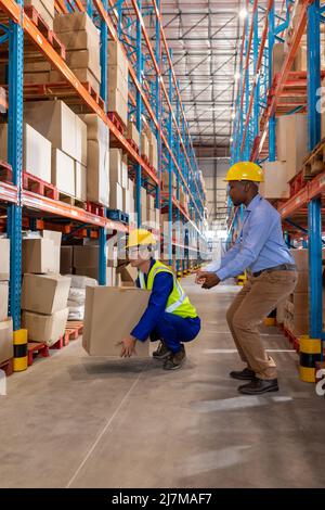 African american young foreman gesturing while guiding asian mature man lifting cardboard box Stock Photo