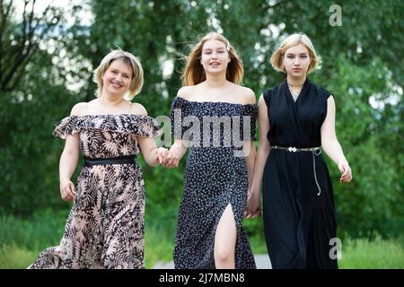 A happy mother with two adult daughters walk along the road and smile. Stock Photo