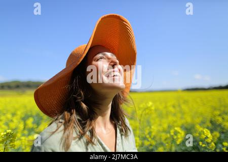 Happy woman wearing orange pamela hat laughing looking above in a field a sunny day Stock Photo