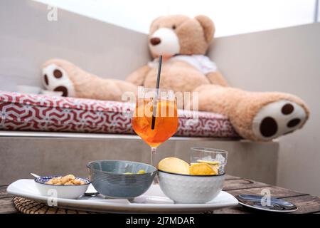 Funny image of a big teddy bear drinking spritz aperitif cocktail drink sitting on the sofa - Party night concept - Focus on red cocktail Stock Photo