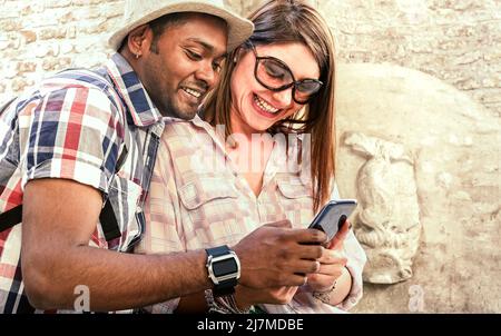 Multiracial couple using mobile smart phone at old town trip - Fun concept with alternative fashion travelers - Indian boyfriend with caucasian girlfr Stock Photo