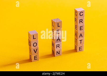 Wooden cubes with the words: love, learn and create on a colorful yellow background. Stock Photo