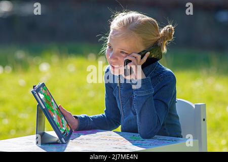 Girl with an i-pad, mobile telephone sitting in the sun receives a lott of radiation this way, from all 3 sources. In physics, electromagnetic radiati Stock Photo