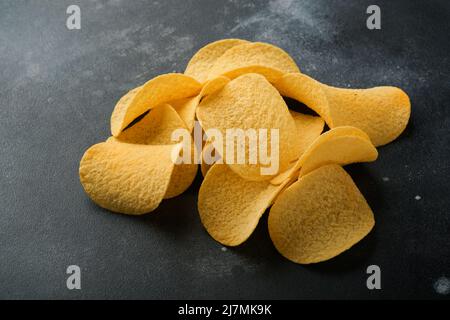 Potato corrugatedchips. Fast food. Crispy potato chips ceramic black bowl with sour cream sauce and onions in wooden stand on old black concrete backg Stock Photo