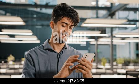 Smiling arabian male professional manager entrepreneur supervisor business man holding smartphone surfing internet touch screen scrolling page on Stock Photo