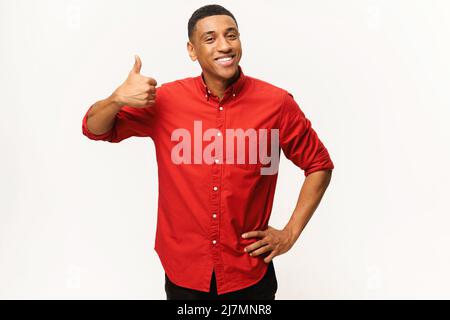 Cheerful African-American guy in red shirt showing thumb up isolated on white. Smiling multiracial man showing approval gesture at the camera, likes it Stock Photo