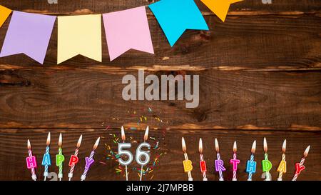 Top view, birthday decorations from candle letters with fire and holiday garlands, copy space. Happy birthday background with number on brown table. Stock Photo