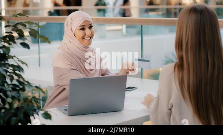 Muslim financial advisor banking worker giving credit card unrecognizable girl client signs contract for approval of bank loan takes mortgage arab Stock Photo