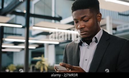 Thoughtful African man professional broker using mobile apps for online sales chatting with friend making order surfing internet focused analyst Stock Photo