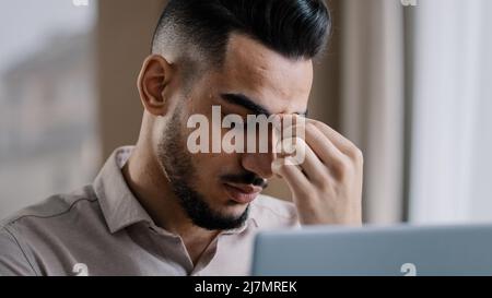 Exhausted young millennial businessman overworked male worker employee massaging dry irritable eyes feeling eyestrain after using computer tired Stock Photo