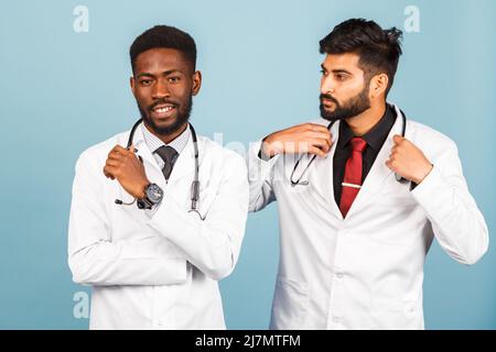 portrait of smiling medical worker in white lab coat with stethoscope conferring with young doctor on blue background Stock Photo