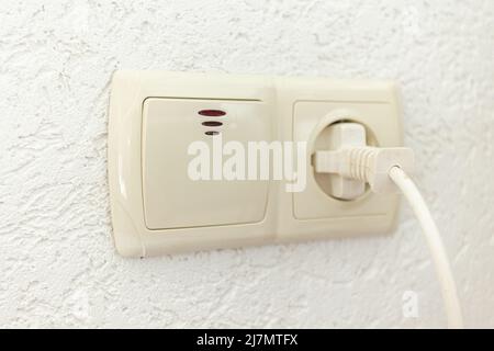 white socket with plug and light switch on an empty wall Stock Photo