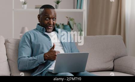 Excited mature man sitting looking at laptop screen reading email with good news rejoices in success celebrating victory actively dancing dance of Stock Photo