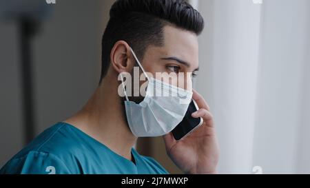 Latin man medical assistant doctor in medical mask consulting patient remote discussing issues by phone hispanic adviser using mobile healthcare app Stock Photo