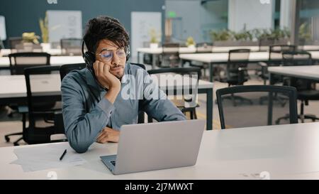Bored man Arabian man Indian service manager in headphones have displeased look video conference webinar learn language improve self-education Stock Photo