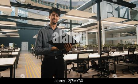 Young indian latin manager male business man employee checking document folder inspecting financial report raising head with satisfied look winking Stock Photo