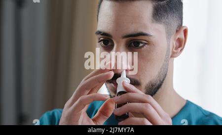 Portrait of sick caucasian man doctor in nurse medical uniform treating runny nose using nasal spray curing snuffle daily therapy from seasonal Stock Photo