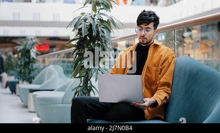 Young serious arab male freelancer in glasses sits looking at laptop screen works remotely loaded in thoughts about work thinks about business problem Stock Photo