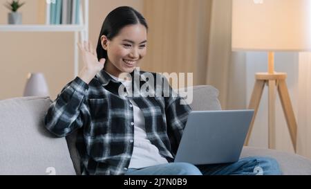 Asian smiling businesswoman freelance student online teacher psychologist girl woman sitting on sofa at home remote talking video call conference app Stock Photo