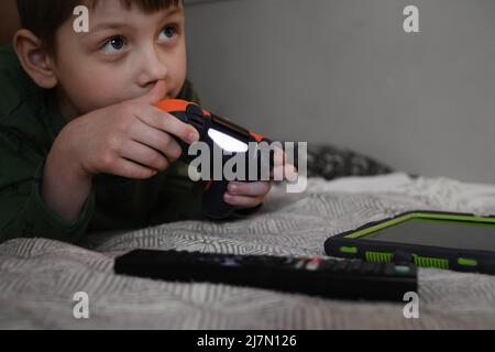Kids playing video games at home on the bed at night. Boys using game console and having fun in the evening. Brothers using technologies exited. Boy Stock Photo