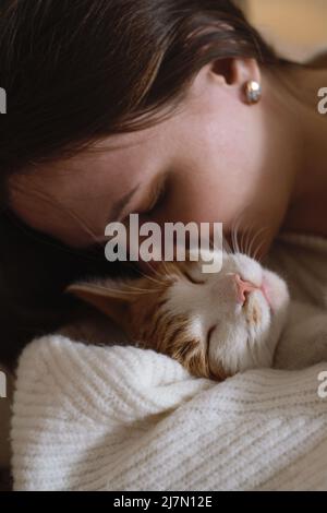 young woman holding cute ginger cat with green eyes. Female hugging her cute short hair kitty in bedroom. Copy space, close up. Adorable domestic pet Stock Photo
