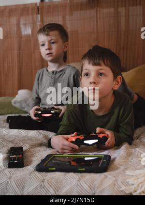 Kids playing video games at home on the bed at night. Boys using game console and having fun in the evening. Brothers using technologies exited. Boy Stock Photo