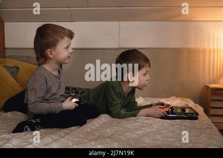Kids playing video games at home on the bed at night. Boys using game console and having fun in the evening. Brothers using technologies exited. Boy Stock Photo
