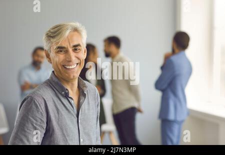 Portrait of happy smiling mature businessman standing against blurred office background Stock Photo