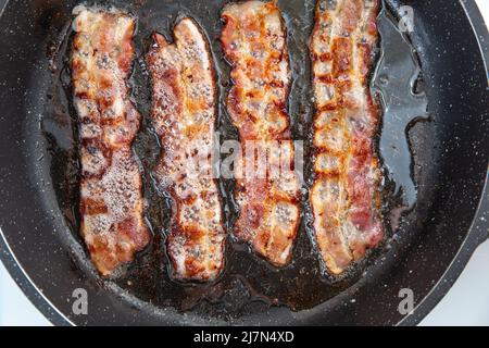 Crispy smokey fried bacon slice or strip. Unhealthy fat food, fattenig ingredient. Red Thin slice or strip or rashers of bacon is fried in a pan, pork Stock Photo