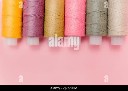 Sewing tools and sewing accessories on elegant pink background. Dressmaking, tailor background. Multicolor sewing threads, thread spools, needles, pin Stock Photo