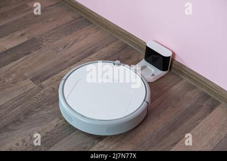 Robotic vacuum cleaner on laminate wood floor charging from base station. Smart cleaning technology. robot vacuum cleaner return to charging at dock Stock Photo