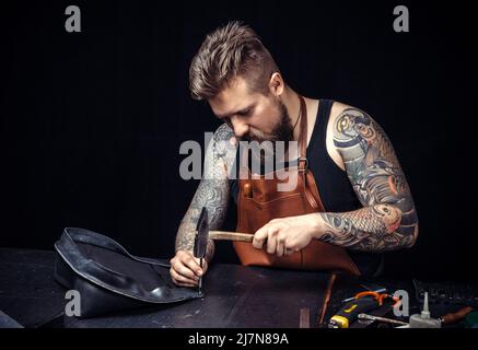 Artist working with leather works with leather goods./Leather workman producing a leatherwork at his workshop. Stock Photo