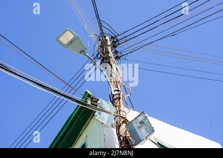 Wooden electric pole with many attached wires, cables and LED street lantern on a blue sky background Stock Photo