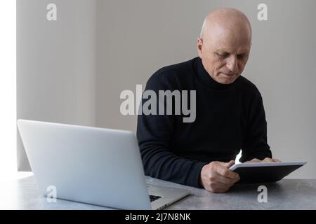 Caucasian old senior stress upset male businessman entrepreneur sitting at working desk having headache after reading graph chart report and contract Stock Photo
