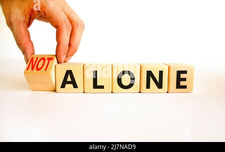 You are not alone symbol. Businessman turns wooden cubes and changes concept words alone to not alone. Beautiful white background. Business, support a Stock Photo