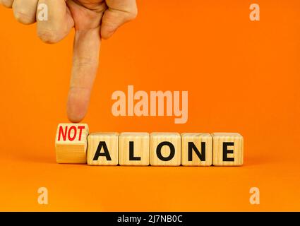 You are not alone symbol. Businessman turns wooden cubes and changes concept words alone to not alone. Beautiful orange background. Business, support Stock Photo