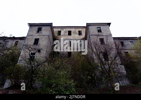 An old abandoned stone building is collapsing in the open air. A depressing view of a dilapidated old stone building with broken windows Stock Photo