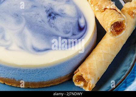 Cheesecake with blueberries and confectionery tubes with condensed milk on a blue plate. Close-up. Stock Photo