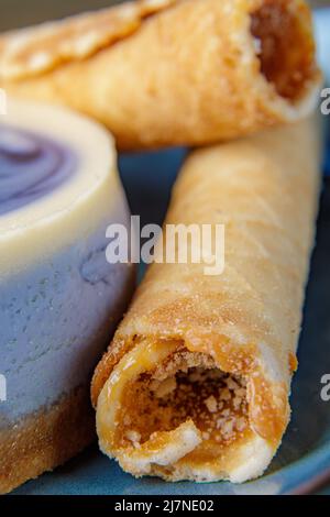 Cheesecake with blueberries and confectionery tubes with condensed milk on a blue plate. Close-up. Stock Photo