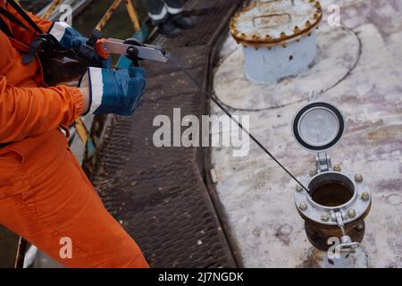 Young offshore engineer sounding fuel oil cargo tank on cargo deck on supply vessel in harbor Stock Photo