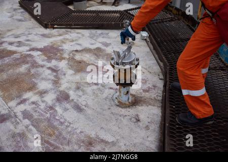 Young offshore engineer sounding fuel oil cargo tank on cargo deck on supply vessel in harbor Stock Photo