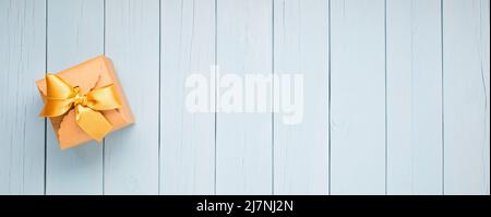 Kraft cardboard gift box with gold ribbon on blue wooden planks Stock Photo