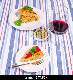 Traditional Spanish starter tortilla patatas served with red piquillo pepper,  olives and spicy guindillas and a glass of red wine. Stock Photo