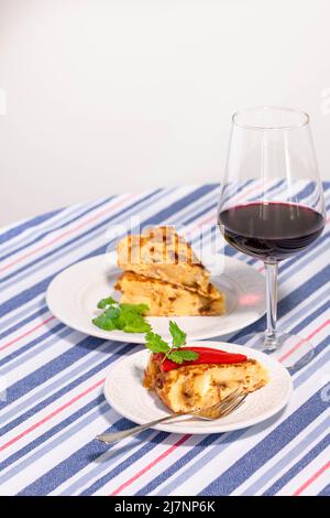 Traditional Spanish starter tortilla patatas served with red piquillo pepper,  olives and spicy guindillas and a glass of red wine. Stock Photo