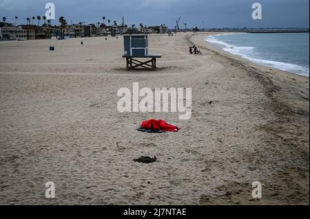 Photo of a person in a red sleeping bag lying on the beach near the municipal pier in this coastal enclave. Stock Photo