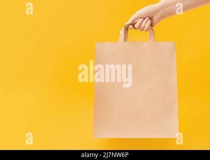 Woman is holding paper bag with handles on yellow backdrop Stock Photo