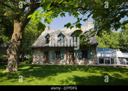 Old 1740 Canadiana fiieldstone home with blue trim and cedar wood shingles roof in summer. Stock Photo