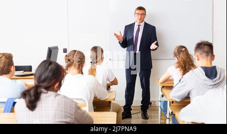 Man teacher with notebook is giving interesting lecture for students in classroom Stock Photo