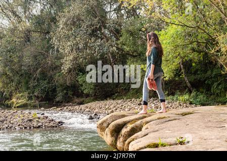 Woman walking on rocks barefooted with her shoes in hands Stock Photo