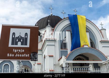 PRODUCTION - 26 April 2022, Brazil, Prudentópolis: A flag of Ukraine hangs on the church 'Sao Josafat' next to a sign with the name of the church in Portuguese. Because Prudentopolis is remote and religiosity is strong, the culture and language of migrants from Ukraine have endured. Russia's attack on Ukraine has sent refugees to the other side of the world. In Brazil, some of them have found a piece of home and the influences of earlier Ukrainian immigrants. (to dpa: 'War refugees in the south of Brazil - 'Little Ukraine' is growing') Photo: Henry Milleo/dpa Stock Photo